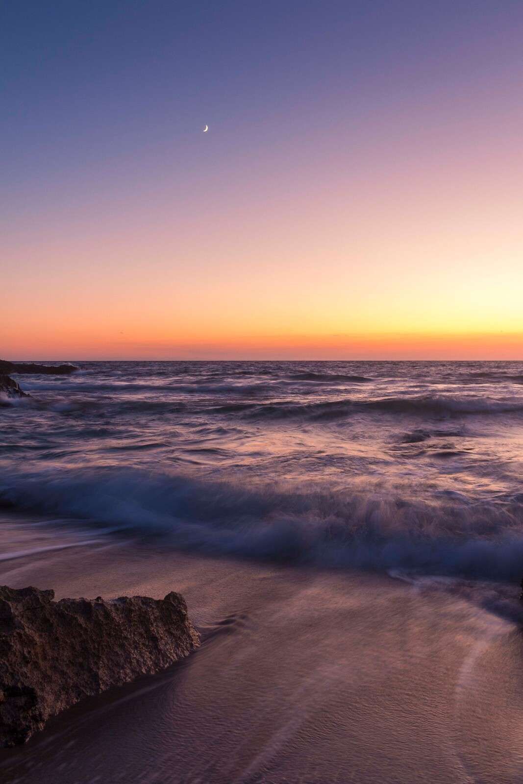 Mondlicht über lila Wellen bei Sonnenuntergang.